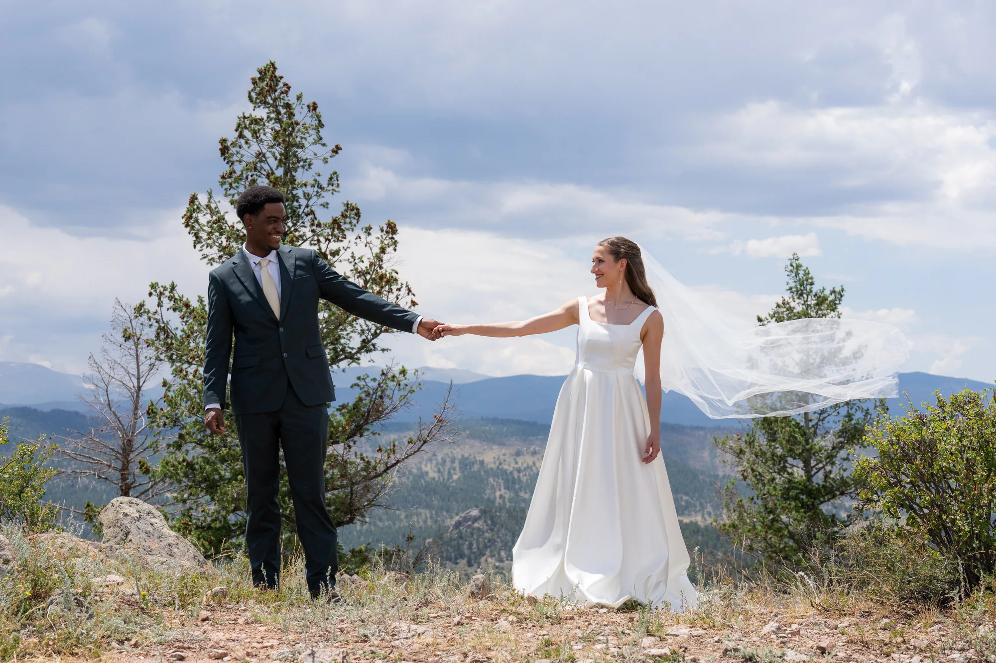 Wide wedding portrait of Isabella and Tim holding hands against a Colorado mountain view